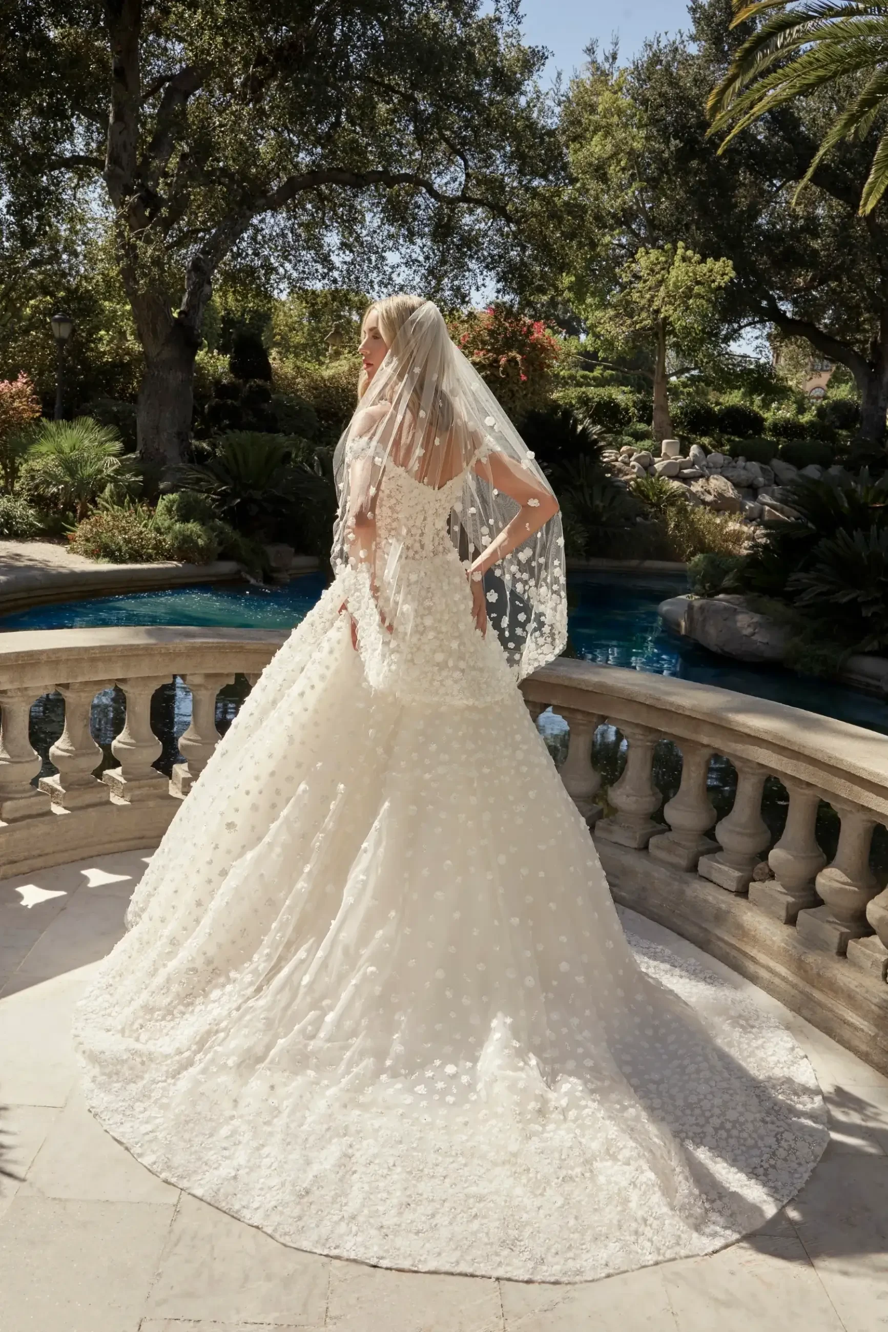 Model is wearing an A-line gown with off-the-shoulder straps, floral appliqués, beading, and an 80” train.