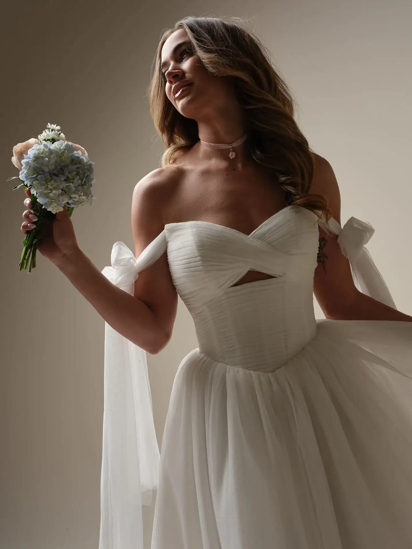 Bride in an elegant white gown holding a bouquet of blue and white flowers. Her expression is joyful, with soft lighting highlighting the scene.