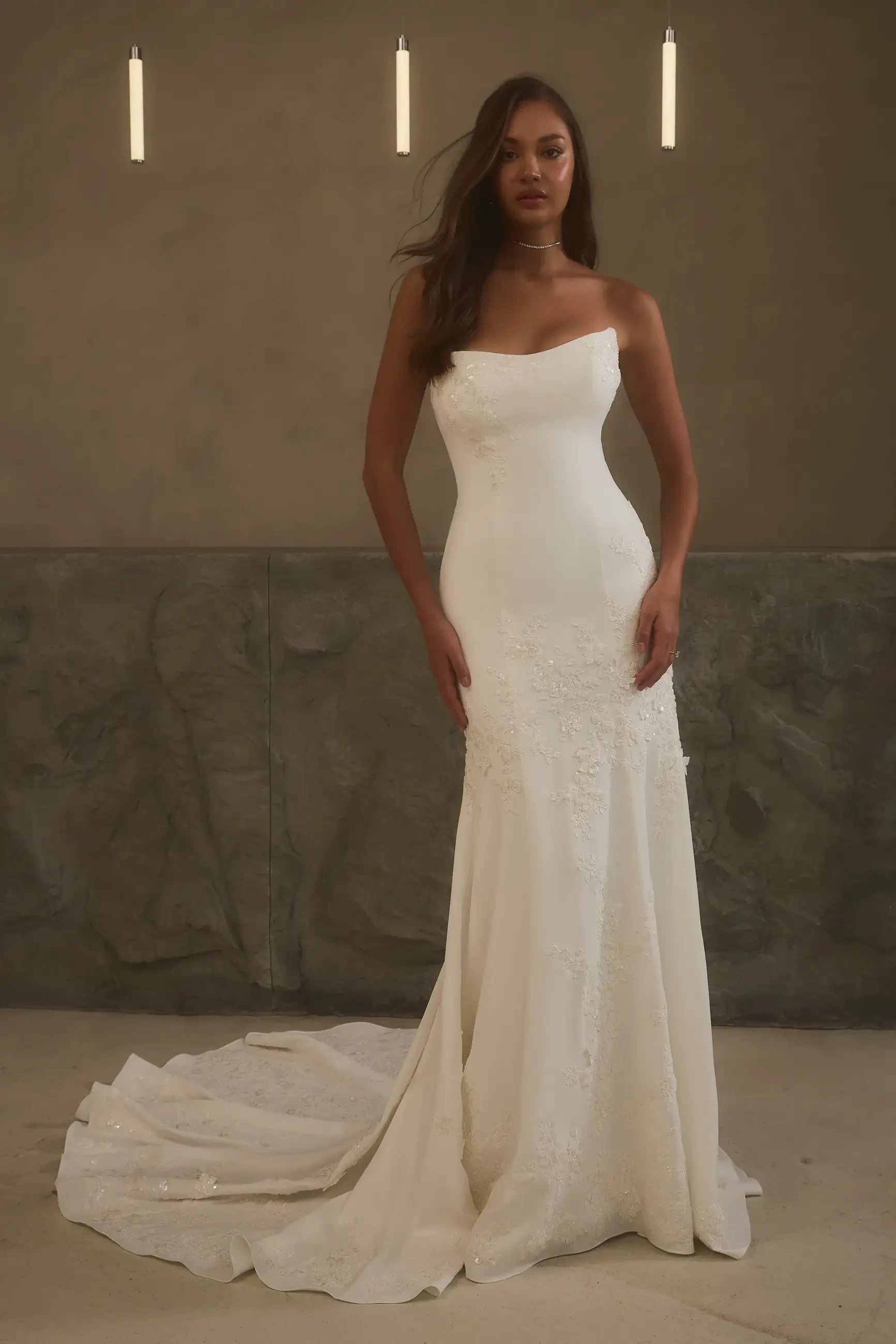 A model wearing a strapless white wedding gown standing against a neutral background.
