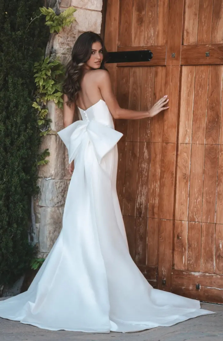Model is wearing a strapless mikado wedding dress with an oversized bow on the back